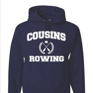 Puede incluir: Sudadera con capucha azul marino con las palabras "COUSINS ROWING" en letras blancas. El diseño incluye una corona, remos cruzados y una corona de laurel. La sudadera tiene un bolsillo delantero y una capucha con cordón.