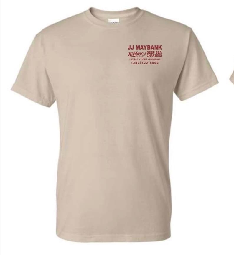 May include: A beige short-sleeved t-shirt featuring red text on the upper left chest that reads JJ MAYBANK, Kildare Island DEEP SEA CHARTERS, LIVE BAIT TACKLE PROVISIONS, and the phone number (252) 522-5502 in a clean, sans-serif font style.