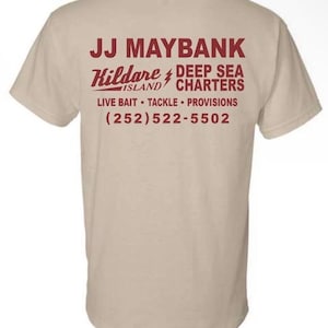 May include: A beige short-sleeve t-shirt featuring dark red text on the back that reads JJ MAYBANK, Kildare Island, DEEP SEA CHARTERS, LIVE BAIT, TACKLE, PROVISIONS, and the phone number (252) 522-5502 with a lightning bolt graphic between the words.