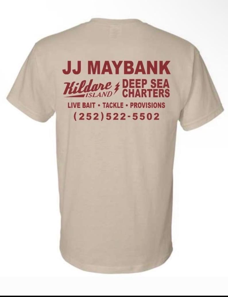 May include: A beige short-sleeve t-shirt featuring dark red text on the back that reads JJ MAYBANK, Kildare Island, DEEP SEA CHARTERS, LIVE BAIT, TACKLE, PROVISIONS, and the phone number (252) 522-5502 with a lightning bolt graphic between the words.