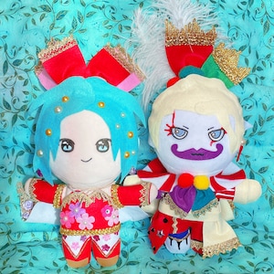 May include: Two plush dolls with detailed costumes and facial features. One doll has blue hair, a red outfit with floral accents, and a large red bow. The other doll has blonde hair, a white and red outfit, and a purple moustache. Both dolls have elaborate headwear.