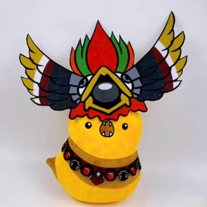 Puede incluir: Una criatura de peluche amarilla con forma de pájaro con un tocado y un collar decorativos. El tocado presenta detalles rojos, verdes, amarillos, negros y blancos. El collar es marrón con detalles rojos. El pájaro tiene un pico pequeño.