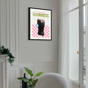 K&ouml;nnte beinhalten: Gerahmter Kunstdruck mit einem Pint Guinness und dem Text "Lovely Day for a Guinness". Das Kunstwerk hat einen rosa-wei&szlig; karierten Hintergrund und einen blauen Aufkleber. Der Druck ist in einem schwarzen Rahmen.