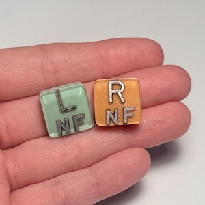 May include: Two square resin tiles with rounded corners. One tile is light green with silver-colored letters L and NF stacked vertically. The other tile is orange with silver-colored letters R and NF stacked vertically. The tiles have a smooth finish.