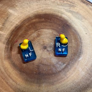 May include: Two blue and white plastic gear shift knobs with yellow duck figurines on top. The knobs are labeled "L NF" and "R NF".