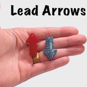 May include: Two arrow-shaped objects, one red and one blue with glitter, are displayed. The red arrow points up, while the blue arrow points down. The text "Lead Arrows" is above the arrows.