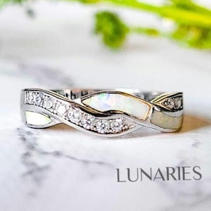 May include: A silver-toned ring with an interwoven design. The ring features a row of small, clear stones and sections of white opal. The word "LUNARIES" is printed at the bottom of the image.