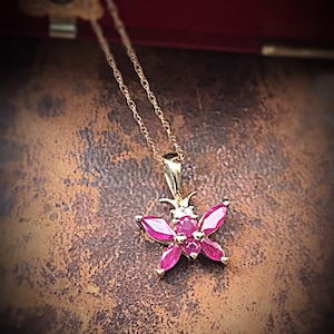 May include: A gold chain necklace with a pendant shaped like a butterfly. The butterfly is adorned with pink gemstones and a few smaller white gemstones.