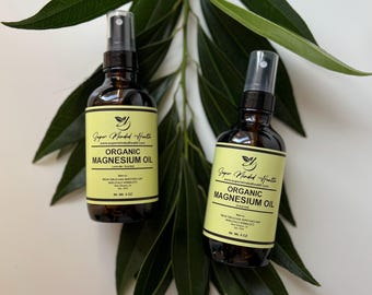 Könnte beinhalten: Zwei bernsteinfarbene Glasflaschen mit Sprühköpfen, beschriftet mit "Super Minded Health Organic Magnesium Oil" mit gelbem Hintergrund und schwarzem Text. Die Flaschen stehen auf einer grünen, blättrigen Oberfläche.