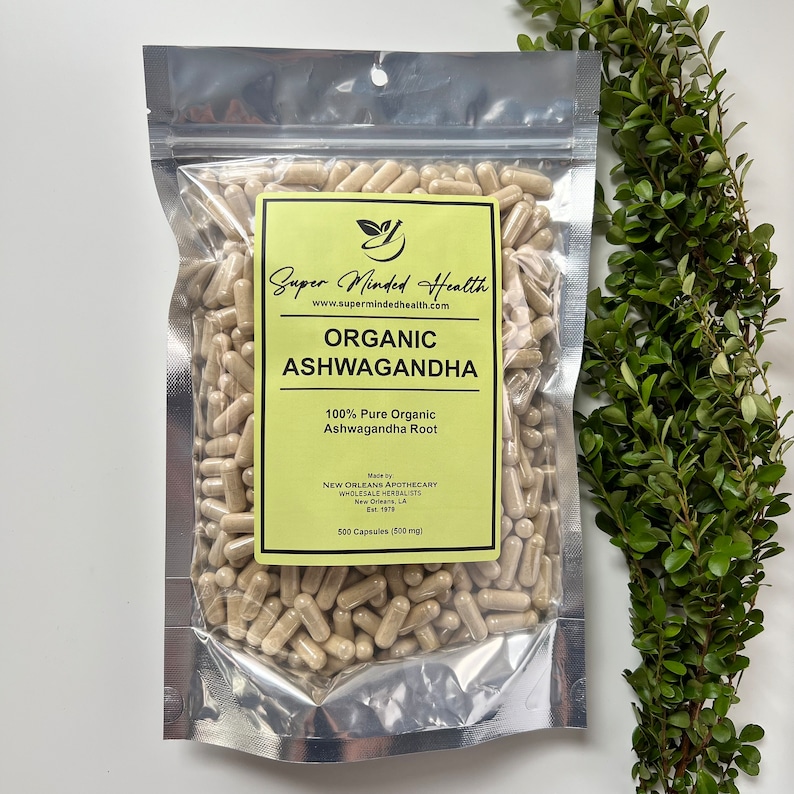 May include: A silver resealable bag filled with 500 capsules of organic ashwagandha root. The bag has a yellow label with the text "Super Minded Health" and "Organic Ashwagandha". The label also states "100% Pure Organic Ashwagandha Root" and "Made by New Orleans Apothecary Wholesale Herbalists Est. 1978".