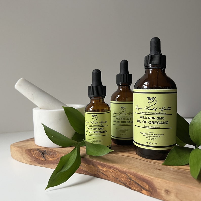 May include: Three amber glass bottles with droppers containing wild-non GMO oil of oregano. The bottles are labeled "Super Minded Health" and have a green leaf logo. The bottles are on a wooden surface with green leaves.