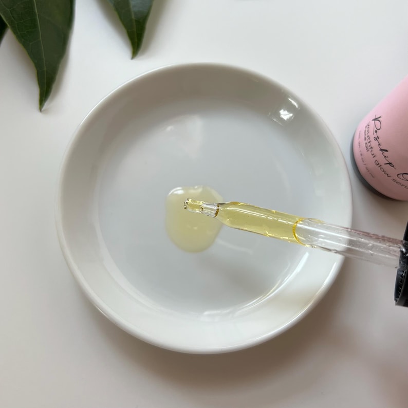 May include: A clear glass dropper bottle with a pink label that says "Radiant Glow Serum". A drop of serum is being dispensed from the dropper onto a white ceramic dish.