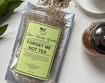 May include: A clear plastic bag filled with a blend of dried herbs labelled "Forget Me Not Tea" by Super Minded Health. The label is yellow with green text and a small green logo. The bag is sitting on a white surface with a teacup and teapot in the background.