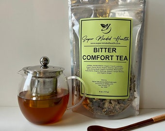 Peut inclure: Une théière en verre avec un infuseur et un couvercle en acier inoxydable, remplie de thé infusé. Un sachet transparent de Bitter Comfort Tea et une cuillère en bois sont à côté de la théière. Le sac porte l'inscription "Bitter Comfort Tea".