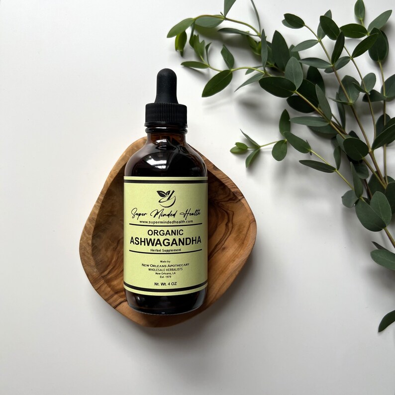 May include: A dark brown glass bottle with a dropper top, containing organic Ashwagandha herbal supplement. The bottle is labelled "Super Minded Health" and "Organic Ashwagandha". It is sitting on a wooden tray.