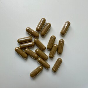 Puede incluir: Un grupo de c&aacute;psulas marrones sobre una superficie blanca. Las c&aacute;psulas son todas del mismo tama&ntilde;o y forma, y est&aacute;n dispuestas en un patr&oacute;n aleatorio.