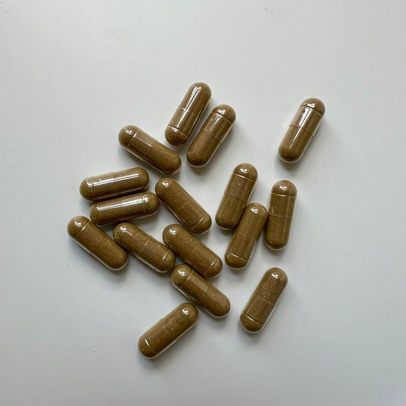 Puede incluir: Un grupo de c&aacute;psulas marrones sobre una superficie blanca. Las c&aacute;psulas son todas del mismo tama&ntilde;o y forma, y est&aacute;n dispuestas en un patr&oacute;n aleatorio.