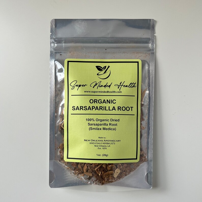 Puede incluir: Una bolsa plateada con una etiqueta amarilla y negra que dice "Super Minded Health" y "Ra&iacute;z de Sarsaparilla Org&aacute;nica". La etiqueta tambi&eacute;n indica "100% Ra&iacute;z de Sarsaparilla Seca Org&aacute;nica (Smilax Medica)" y "Hecho por New Orleans Apothecary Wholesale Herbalists Est. 1979". La bolsa contiene ra&iacute;z de sarsaparilla seca.