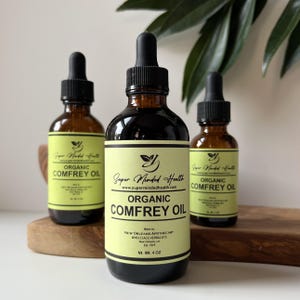 May include: Three amber glass bottles with dropper tops filled with a dark liquid. The bottles are labeled "Organic Comfrey Oil" and feature the brand name "Super Minded Health".