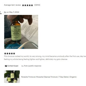 May include: A glass bottle with a brown liquid and a label that reads "Organic Parasite". The bottle is being held by a hand. The image is a product review for a parasite cleanse tincture.