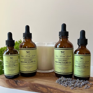May include: Four amber glass bottles with dropper tops containing organic magnesium oil. The bottles are labelled "Super Minded Health" and have a green leaf logo. The bottles are arranged on a wooden surface with lavender flowers scattered around them. The bottles are available in 2 oz and 4 oz sizes.
