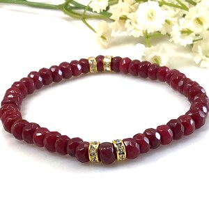 May include: A red beaded bracelet with gold accents and clear crystal embellishments.