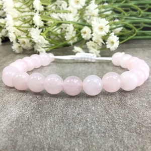 May include: A pink rose quartz beaded bracelet with a white cord closure.