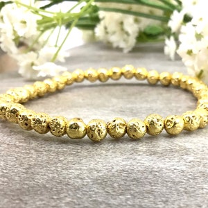 May include: A gold lava rock beaded bracelet. The beads are small and round, with a textured surface.