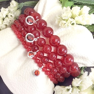 May include: Four red gemstone bracelets with silver charms. Each bracelet features round red beads and a silver charm with a red gemstone.
