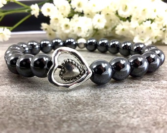 May include: A black hematite beaded bracelet with a silver heart charm. The heart charm has a smaller heart inside of it.