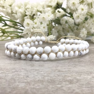 May include: A white howlite beaded bracelet with a beige cord. The bracelet is double-layered and has a simple design.