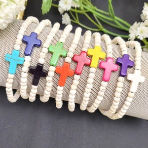 May include: A set of ten bracelets with white beads and colorful cross charms. The charms are turquoise, blue, black, red, green, yellow, pink, purple, and white.