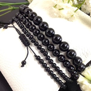 May include: Four black beaded bracelets with adjustable string closures. The bracelets are made of round, polished black beads of varying sizes.