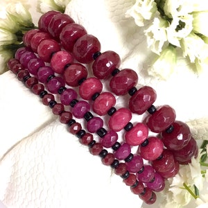 May include: A set of four red gemstone bracelets with black beads. The bracelets are made of faceted, round beads and are stacked on top of each other.