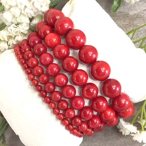 May include: A set of six red coral bead bracelets, each with a different size bead. The bracelets are stacked on top of each other, creating a visually appealing display.