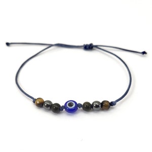 May include: A blue string bracelet with a blue evil eye charm, brown tiger's eye beads, and black hematite beads.