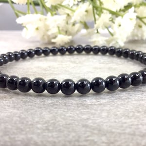 May include: A black beaded bracelet made with small, round, polished beads.