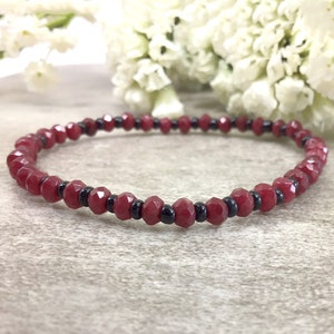 May include: A red and black beaded bracelet. The bracelet is made with small, faceted red beads and black beads.