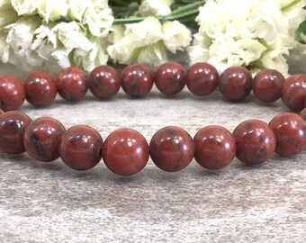 May include: Red jasper beaded bracelet with a dark red and black marbled pattern. The bracelet is made of round beads and is approximately 7 inches in length.