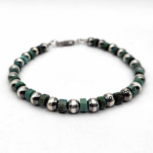 May include: A silver and turquoise beaded bracelet with a silver clasp. The bracelet has a mix of round and square beads.