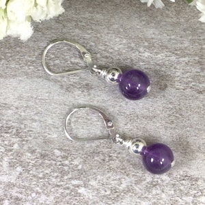 May include: A pair of silver earrings with a purple amethyst gemstone bead on each earring.