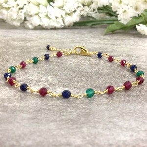 May include: Gold-toned bracelet featuring a delicate chain interspersed with faceted beads in shades of red, blue, and green. The bracelet has a lobster clasp closure and is displayed against a neutral background.