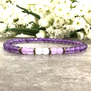 May include: A purple amethyst bracelet with two light purple and one white beads, accented with gold-toned spacers.