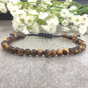 May include: A brown and gold tiger's eye beaded bracelet with a black cord and adjustable knot closure.