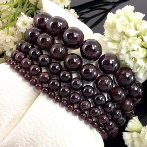 May include: A set of six garnet gemstone bracelets, each with a different size of round beads. The bracelets are stacked on top of each other, showing the different sizes of the beads.
