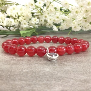 May include: Red gemstone bracelet with a silver charm featuring a red gemstone. The bracelet is made of round red beads.