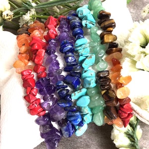 May include: Seven colorful gemstone bracelets stacked on top of each other. The bracelets are made of small, irregular shaped chips of carnelian, red coral, amethyst, lapis lazuli, turquoise, aventurine, and tiger's eye.