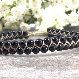 May include: Black onyx bead bracelet with a braided gold cord. The bracelet is adjustable with a sliding knot.