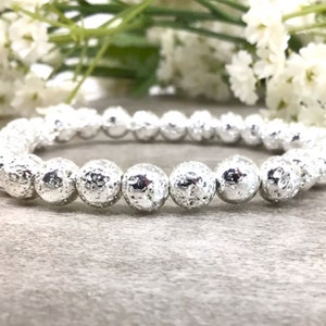 May include: A stretch bracelet composed of round, silver-colored beads with a porous, textured surface. The beads are uniform in size and arranged in a single continuous loop, creating a metallic appearance that reflects light across the surface.