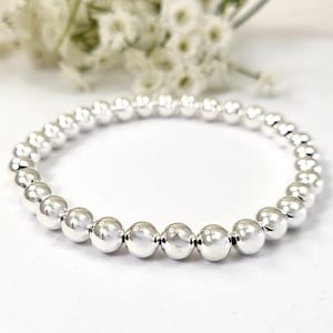 May include: A silver beaded bracelet with a simple design. The bracelet is made of round, smooth beads that are strung together on a stretchy cord.